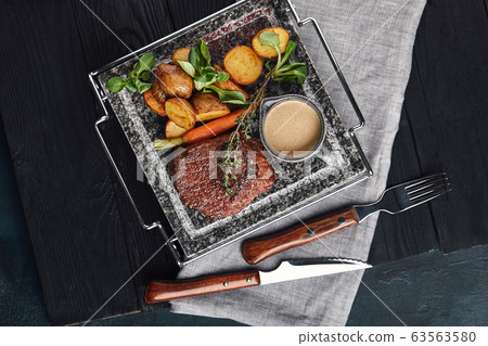 Meat steak with baked baby potatoes and vegetables on a marble plate. Italian cuisine, top view, dark background. Food photo, delicious food 63563580