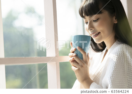 Woman holding a mug relaxing indoors Woman holding a mug relaxing indoors 63564224