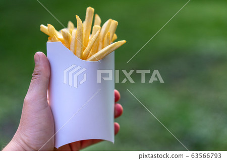 Tasty juicy french fries in white paper box in man Tasty juicy french fries in white paper box in man 63566793