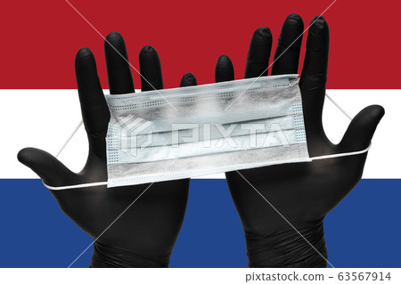 Doctor holds face mask in hands in black medical gloves on background colors flag of Netherlands. Concept coronavirus quarantine Doctor holds face mask in hands in black medical gloves on background colors flag of Netherlands. Concept coronavirus quarantine 63567914
