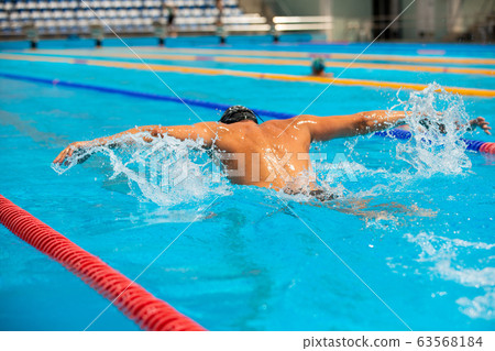 Athletic man swimming in butterfly style in the swimming pool with clear blue water. 63568184