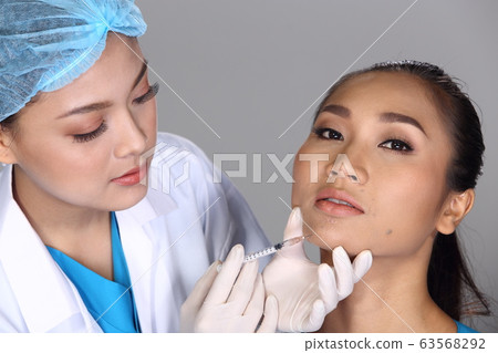 Asian Doctor Nurse check face cheek bone structure before plastic surgery and inject beauty chemical syringe to patient with acne, wart, Studio lighting grey background 63568292