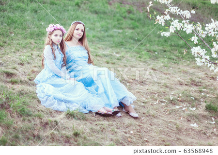 Mom and daughter are sitting near the blooming 63568948