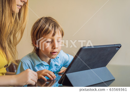 A boy studying online at home using a tablet. Mom helps him learn. Studying during quarantine A boy studying online at home using a tablet. Mom helps him learn. Studying during quarantine 63569361