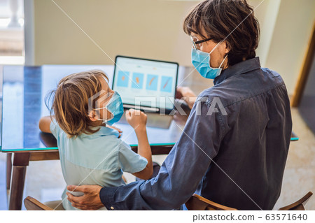 Boy studying online at home using a tablet. Father helps him learn. Father and son in medical masks Boy studying online at home using a tablet. Father helps him learn. Father and son in medical masks 63571640