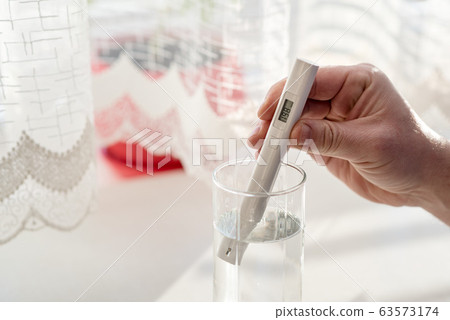 Process of checking the purity level of tap water using water TDS meter tool, close up. Device shows 198 ppm of contaminant level, which is considered the typical value. At home in the kitchen 63573174