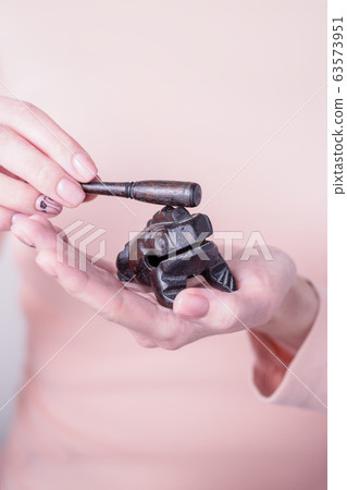 Beautiful female hands holding black wooden ratchet money toad on a light background. Prosperity concept Beautiful female hands holding black wooden ratchet money toad on a light background. Prosperity concept 63573951