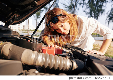 Woman checking car engine after breakdown Woman checking car engine after breakdown 63574324