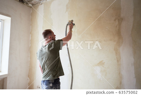 Man painting with airbrush apartment repairment against small window in the daytime Man painting with airbrush apartment repairment against small window in the daytime 63575002