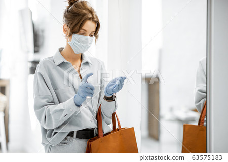 Woman in medical mask and gloves disinfecting hands after coming home 63575183