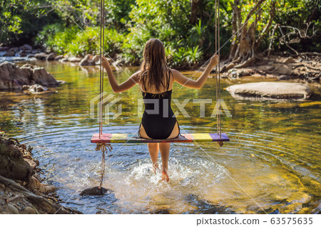 Beautiful happy girl, young pretty cheerful woman traveler sitting, swinging on a swing tied to a Beautiful happy girl, young pretty cheerful woman traveler sitting, swinging on a swing tied to a 63575635