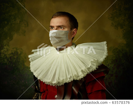 Young man as a medieval knight on dark background wearing protective mask against coronavirus 63578376