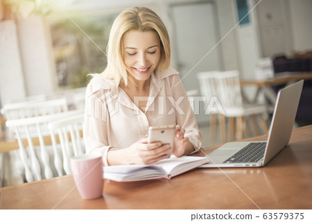 Young woman in cafe sitting browsing smartphone smiling joyful 63579375