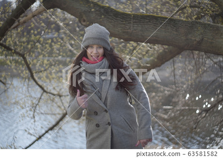 Cheerful brunette grey-eyed girl showing thumb up outdoors. Portrait of joyful cute Caucasian woman having fun in park on sunny autumn day. Leisure, lifestyle, happiness, joy. Cheerful brunette grey-eyed girl showing thumb up outdoors. Portrait of joyful cute Caucasian woman having fun in park on sunny autumn day. Leisure, lifestyle, happiness, joy. 63581582