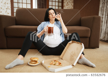 Pregnant woman with belly smoking and drinks beer Pregnant woman with belly smoking and drinks beer 63582676