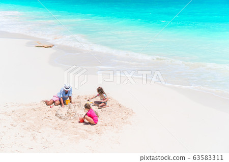 Father and little daughters making sand castle at tropical beach Father and little daughters making sand castle at tropical beach 63583311