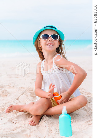 Little girl with bottle of sun cream sitting at tropical beach 63583316