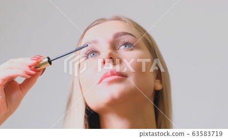 Pretty blond woman applying mascara make-up on her eyelashes in front of mirror. Beauty and makeup 63583719