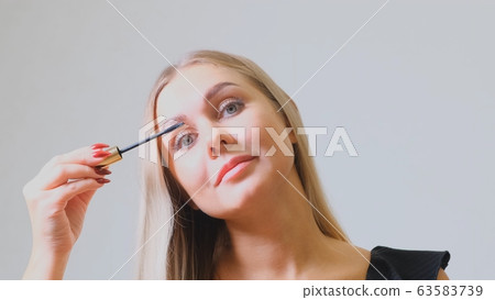 Pretty blond woman applying mascara make-up on her eyelashes in front of mirror. Beauty and makeup Pretty blond woman applying mascara make-up on her eyelashes in front of mirror. Beauty and makeup 63583739