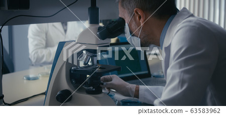 Scientist studying sample in microscope 63583962