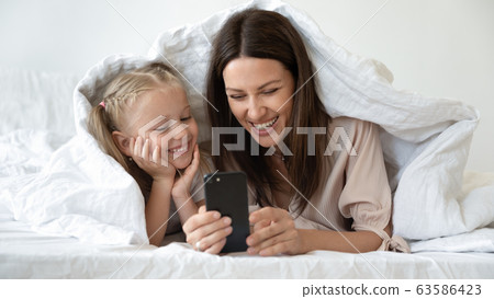 Happy mom and daughter watch cartoon under blanket 63586423