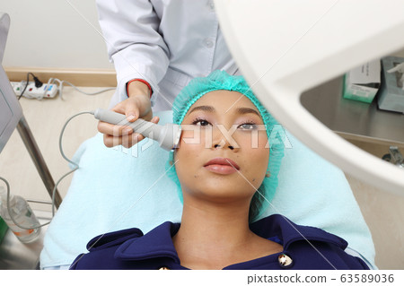 Treatment on Asian Woman as patient to make skin smooth bright and cure acne with medical beauty device instrument high frequency on face in hospital clinic 63589036