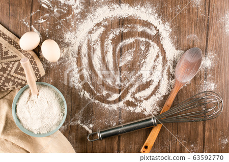 A bowl of flour with eggs and wooden spoon 63592770