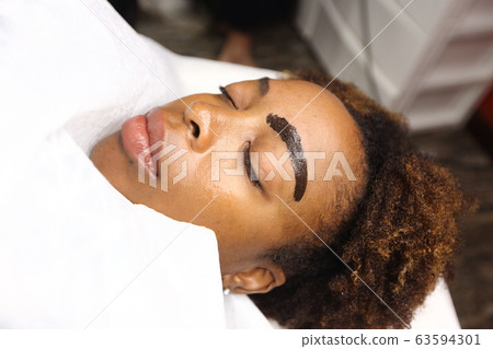 Professional Beautician woman applying Tottoo, Brow Microblading to Black african customer eyebrows to make permanent color makeup or tattooing line look real in beauty salon, copy space for text log Professional Beautician woman applying Tottoo, Brow Microblading to Black african customer eyebrows to make permanent color makeup or tattooing line look real in beauty salon, copy space for text log 63594301