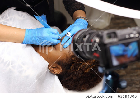 Professional Beautician woman applying Tottoo, Brow Microblading to Black african customer eyebrows to make permanent color makeup or tattooing line look real in beauty salon, copy space for text log Professional Beautician woman applying Tottoo, Brow Microblading to Black african customer eyebrows to make permanent color makeup or tattooing line look real in beauty salon, copy space for text log 63594309