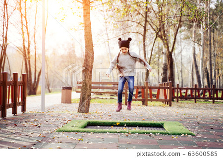 Happy school girl jumping on a small trampoline in the park Happy school girl jumping on a small trampoline in the park 63600585