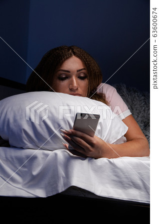 Young woman using phone at night in the bed at home. Insomnia concept. 63600674