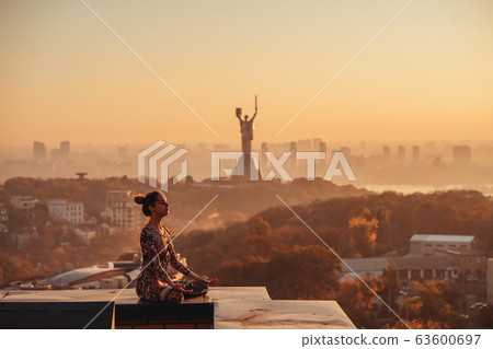 Woman doing yoga on the roof of a skyscraper in big city. 63600697