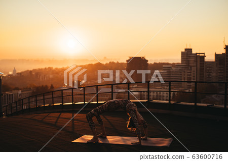 Woman doing yoga on the roof of a skyscraper in big city. 63600716