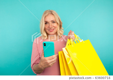 Happy adult female holding phone and yellow bags. Happy adult female holding phone and yellow bags. 63600718