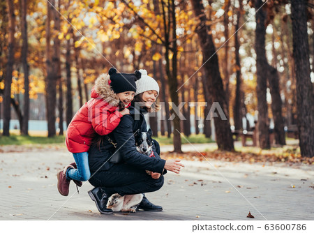 Happy mother and her daughter playing with dog in autumn park Happy mother and her daughter playing with dog in autumn park 63600786