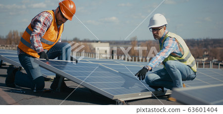 Technicians installing solar panels on metal stand 63601404