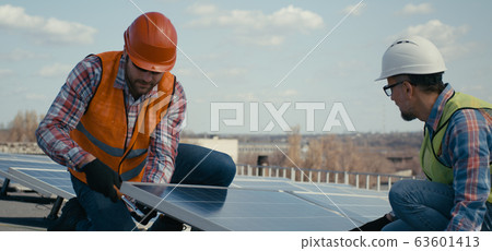 Technicians installing solar panels on metal stand 63601413