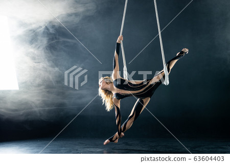 A young girl performs the acrobatic elements in the air trapeze. Studio shooting performances on a black background 63604403
