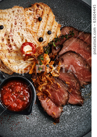 Juicy roast beef with ciabatta in tomato sauce is beautifully sliced and laid out on plates. top view, beautiful table setting, beautiful serving, traditional italian food, gray background, copy space Juicy roast beef with ciabatta in tomato sauce is beautifully sliced and laid out on plates. top view, beautiful table setting, beautiful serving, traditional italian food, gray background, copy space 63604445