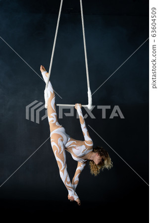 A young girl performs the acrobatic elements in the air trapeze. Studio shooting performances on a black background 63604509