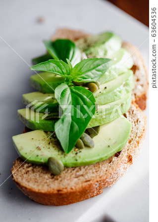 Avocado toast with cherry tomatoes and pepitas on a cutting board. Home cooking, healthy eating concept Avocado toast with cherry tomatoes and pepitas on a cutting board. Home cooking, healthy eating concept 63604536