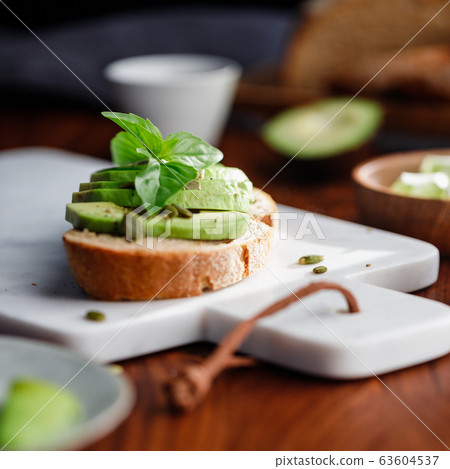 Avocado toast with cherry tomatoes and pepitas on a cutting board. Home cooking, healthy eating concept Avocado toast with cherry tomatoes and pepitas on a cutting board. Home cooking, healthy eating concept 63604537