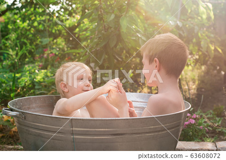 Two brothers bathing in metal basin in village Two brothers bathing in metal basin in village 63608072