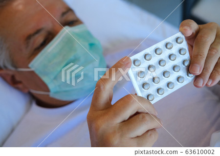 Sick man in bed bed with medical face mask, taking 63610002