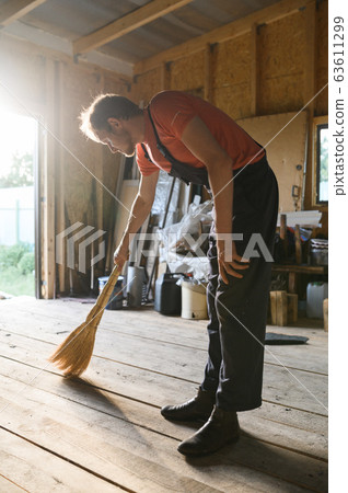 man sweeps the wood floor. barn cleaning 63611299