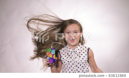 Child with headphones dancing at studio background. Girl listens to music on smartphone. Beautiful cute happy little girl listens to music. 63612869