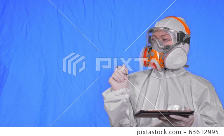 Scientist virologist in respirator makes write in an tablet computer with stylus. Woman wearing protective medical mask. Chroma key blue. 63612995
