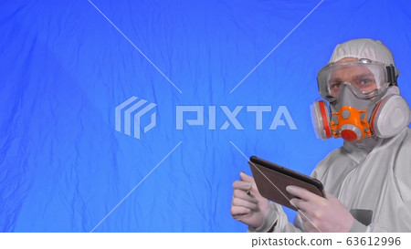 Scientist virologist in respirator makes write in an tablet computer with stylus. Man wearing protective medical mask. Chroma key blue. 63612996