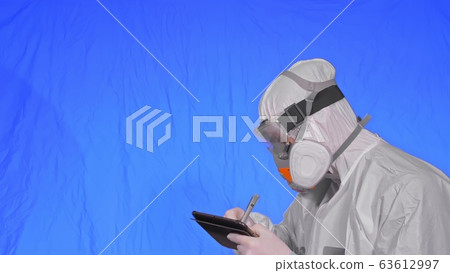 Scientist virologist in respirator makes write in an tablet computer with stylus. Man wearing protective medical mask. Chroma key blue. Scientist virologist in respirator makes write in an tablet computer with stylus. Man wearing protective medical mask. Chroma key blue. 63612997