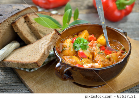 Hot vegetarian potato goulash served in a ceramic bowl with dark baked farmhouse bread  63617151